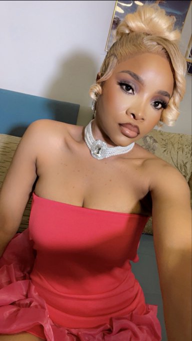 A selfie of a woman with blonde hair in a top knot, wearing a red strapless dress and a sparkly choker necklace.