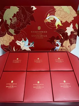 An open red gift box with floral designs on the lid, containing multiple smaller red square packages labeled 'SHANGRI-LA', likely containing mooncakes.