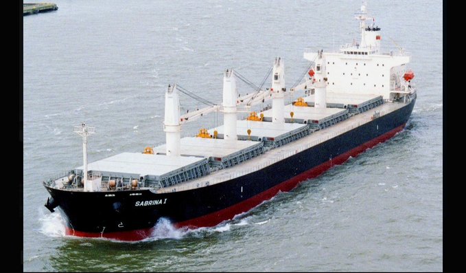 Aerial view of a large black and red bulk carrier ship named "SABRINA I" sailing through water with its cargo cranes visible.