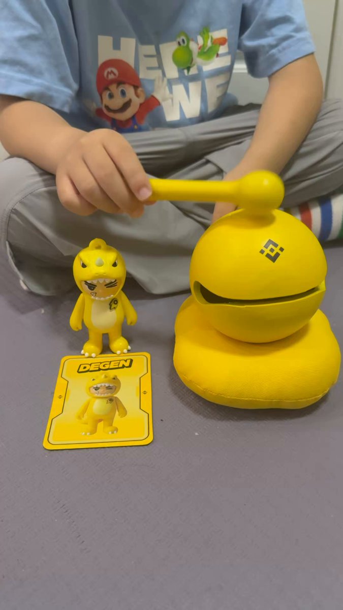 The image features a child sitting on the floor, surrounded by various toys including a yellow toy dinosaur figure, a yellow toy ball, and a yellow toy box with a picture of a baby inside. The child appears to be playing with these toys while wearing a blue shirt. In the background, there is a post that reads "Some people spend their lifetime healing their childhood Some people spend their childhood healing a lifetime Gen-Z little milk dog unboxing video Thanks to Binance @binancezh @binancezh @yayabinance". This suggests that the image might be related to a social media post or a discussion about the importance of play and childhood memories.