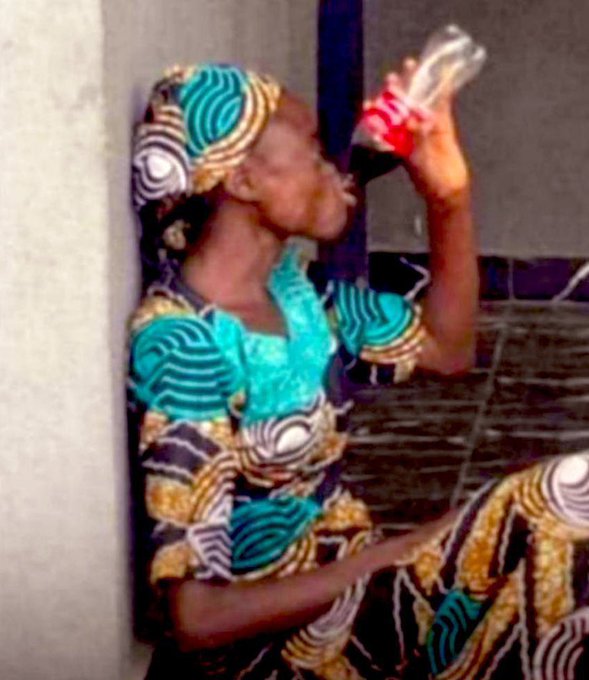 A woman wearing a colorful patterned dress and matching headwrap sits while drinking from a Coca-Cola bottle, her image used to celebrate the return of the CTNG (Côte d'Ivoire).