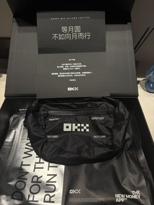 An opened black OKX branded gift box reveals a black pouch with 'TRUSTED VERIFIED' text and a card wishing 'HAPPY MID-AUTUMN FESTIVAL' alongside Chinese characters '等月圆 不如向月而行'.