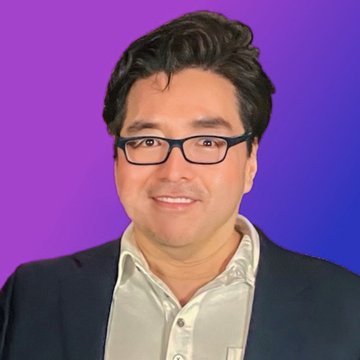 A smiling man with dark hair and black-rimmed glasses wearing a dark blazer over a light shirt, posed against a vibrant purple-to-blue gradient background. The professional portrait accompanies a quote attributed to Tom Lee about the ongoing crypto bull market, suggesting he may be the analyst pictured.