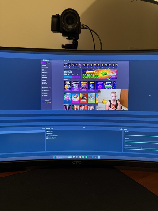A curved KTC ultrawide monitor displays a Twitch livestream of a streamer in a tank top, with a celebratory "NICE 30,000,000!" graphic visible on screen, while a webcam sits mounted above—capturing the moment the streamer's channel hits 30 million views, tying into the welcoming post about the channel @YEET and @cousincrypt0.