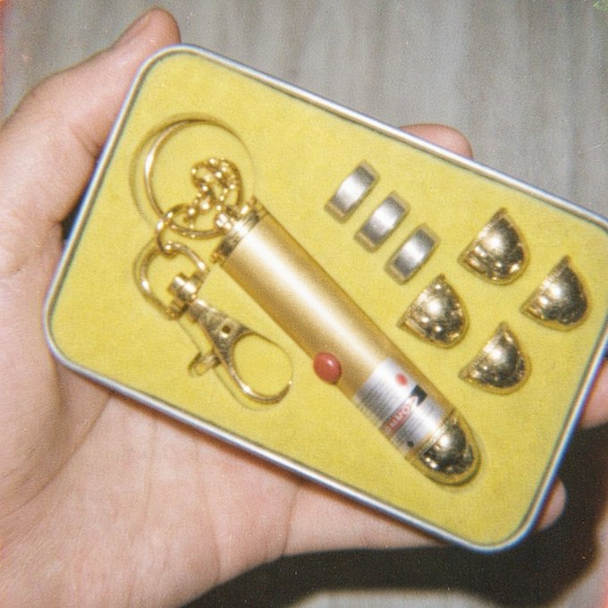 A hand holding a small yellow gift box containing a gold-colored bullet-shaped keychain with a lighter function, along with several gold-toned bullet-shaped charms.