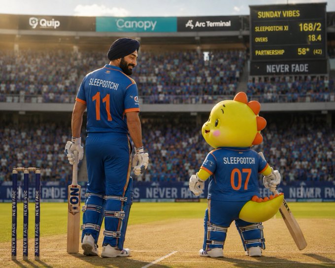 In this image, there are two cricket players standing next to each other with a mascot of a yellow dinosaur holding a bat. The player wearing a blue jersey has the number 11 on his back. They appear to be at a cricket match or practice session. A scoreboard can also be seen in the background, indicating that they might be playing for a team or participating in an event.