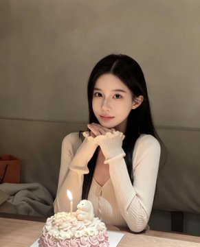 A young woman with long dark hair sits at a table in a cream-colored sweater, hands clasped near her face, smiling softly in front of a lit pink and white frosted birthday cake, celebrating her birthday. The accompanying post wishes herself a happy birthday and asks followers to wish her the same, while also wishing everyone "永不爆仓" (never get margin-called), suggesting the cake marks her special day.
