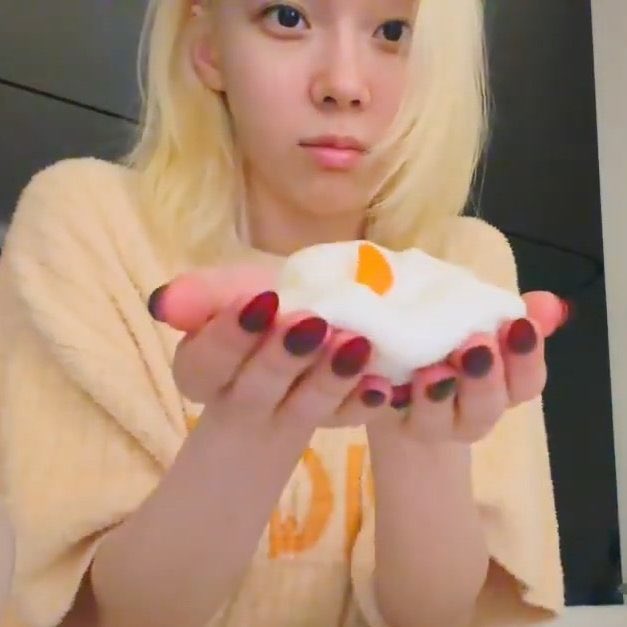 A young woman with blonde hair holds a small, fluffy white dessert with an orange center in her cupped hands, presenting it to the camera with a soft expression. The caption "This is it, baby dog." suggests she's offering the tiny treat affectionately, as if presenting a special find to a loved one.