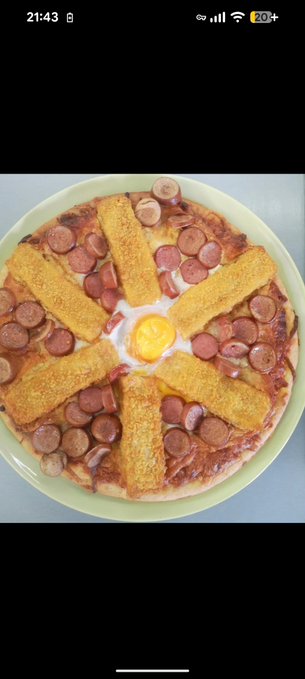 The image features a pizza topped with sausage, egg, and breadcrumbs. The pizza has six slices arranged around a yellow plate, creating an interesting and unique presentation. The background of the photo appears to be black, which contrasts with the colorful toppings on the pizza.