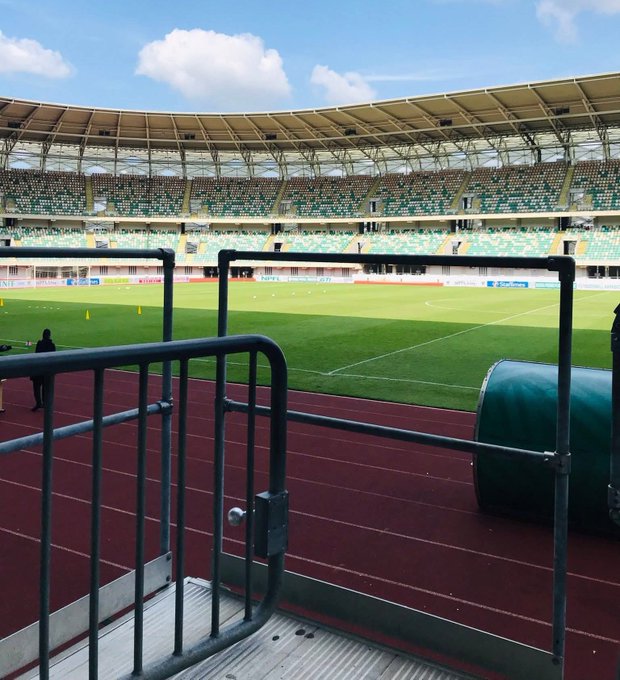 The image shows a stadium filled with people, likely attending an event or gathering. There are several individuals scattered throughout the scene, both near the foreground and background of the picture. A person can be seen standing at the edge of the frame on the left side, while another individual is located closer to the center of the image. The stadium appears to be a popular venue for various activities, with people engaged in different conversations or observing their surroundings.