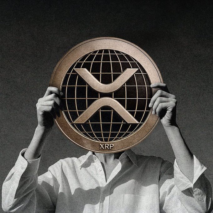 A person wearing a white button-up shirt holds a large bronze XRP cryptocurrency coin (with a globe design and the XRP ticker) in front of their face.
