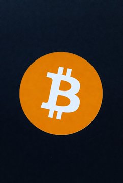 The Bitcoin logo, featuring the iconic orange "₿" symbol on a dark background, visually anchors the post about Standard Chartered's $100,000 end-of-2026 BTC price forecast and Strategy's reliance on Bitcoin to back its STRC preferred stock.