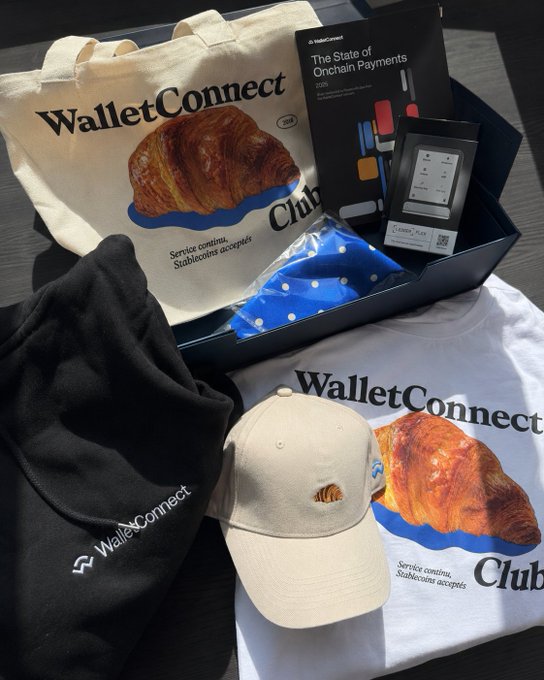 A black and white t-shirt with a croissant design, "WALLET CONNECT" logo, and "Club" text is displayed on a wooden table.