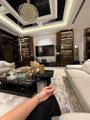 A person relaxes on a light-colored couch in a spacious modern living room with a large sectional sofa and decorative lighting.