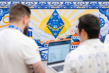 Two individuals focus on a laptop with a vibrant mural of the Ethereum logo and a Portuguese-inspired cityscape behind them, symbolizing the high-stakes finalist judging at ETHGlobal Lisbon. This art visually represents the culmination of the hackathon as seen in the accompanying post.