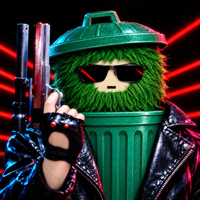 A figure dressed as an anthropomorphic green trash can wearing sunglasses and a studded black leather jacket holds up two handguns against a backdrop of red laser lights, evoking a fierce, action-movie aesthetic that humorously personifies the "$GOR" token mascot ready to make its comeback.