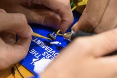 A close-up shot captures hands stitching the blue and yellow border of an FC Barcelona soccer jersey.