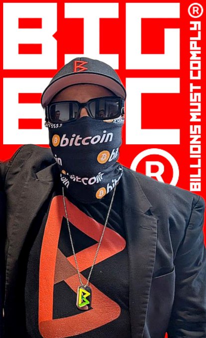 A person wearing sunglasses, a baseball cap, and a Bitcoin-branded face covering, standing in front of a red background with 'BIG' and 'BILLIONS MUST COMPLY' visible, wearing a black jacket with a red Bitcoin logo.