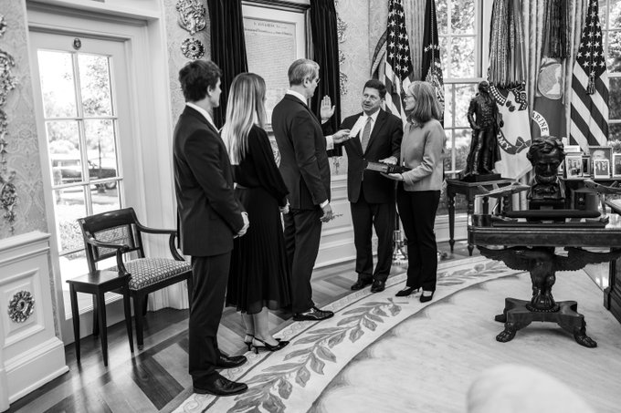The image depicts a group of people, including a smiling man in a suit shaking hands with a man in a dark suit, in what appears to be an official room with American flags in the background, possibly the White House. The accompanying post draws a connection to the individual involved in the Ripple lawsuit and his subsequent appointment as US Director of National Intelligence, suggesting a controversial intersection of legal and political actions.