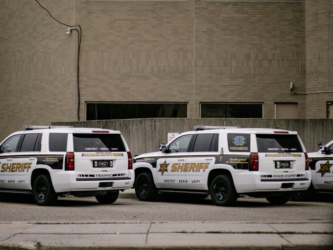 Two parked Sheriff SUVs marked "PROTECT • SERVE • UNIFY" and "Dedicated to Community" sit outside a brick building, visually reinforcing the law enforcement presence tied to the Major County Sheriffs of America's recent shift to neutral on the CLARITY Act.