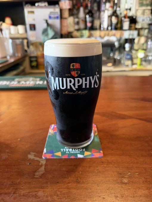 A pint glass of Murphy's Irish Stout beer sitting on a coaster labeled 'COCKTAIL ENGLISH CO.' on a wooden bar counter.