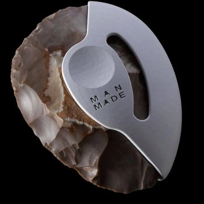 A close-up product photo displays a white tool with 'MAN MADE' engraved on it, resting against a piece of natural stone or crystal on a black background.