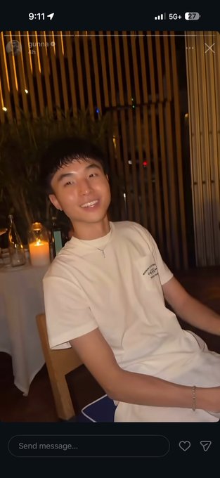 A young man smiles warmly while seated in a dimly lit restaurant with candles and wooden slats in the background, wearing a cream t-shirt and a bracelet. The post's caption about "your favorite rapper posted kimchi" humorously ties to the Asian restaurant setting, suggesting the evening captured a kimchi-related moment with a playful nod to "onchain traders are the new athletes."