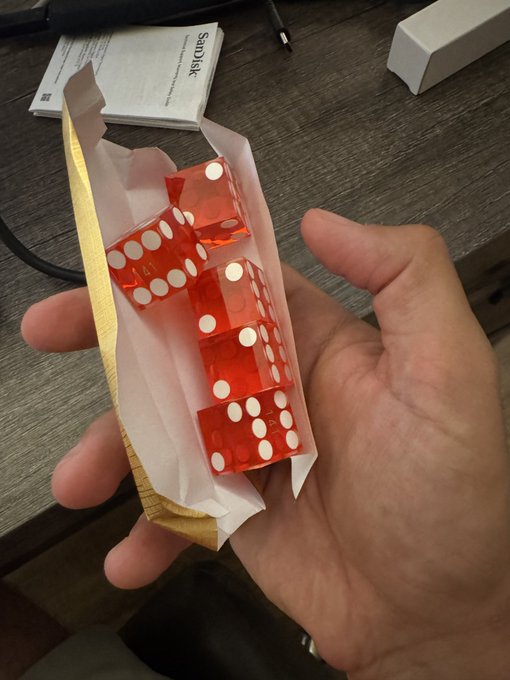 A hand holds a brown paper bag containing three translucent red casino dice with white pips.