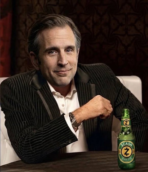 A man in a pinstriped blazer and white shirt sits at a table with a green beer bottle labeled 'Z CASH' featuring a gold 'Z' logo.