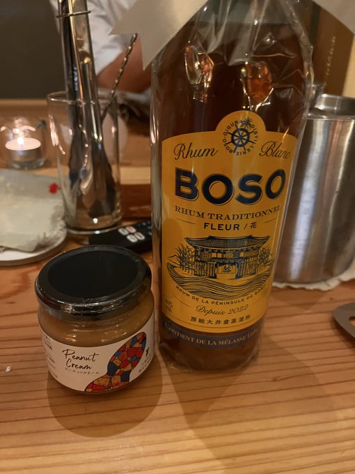 A bottle of Boso Rhum Blanc Traditionnel Fleur alongside a small jar of peanut cream on a wooden table.