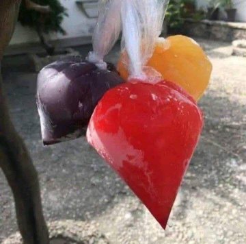 A close-up photo of colorful, translucent fruit-shaped hard candies (strawberry, orange, and grape/purple) hanging in clear plastic wrappers outdoors.