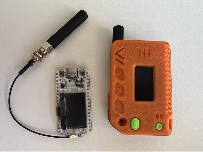 An electronic assembly with an antenna, a clear circuit board with an OLED screen, and an orange 3D-printed case labeled 'H1' are displayed on a white surface.