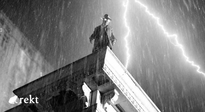 A black-and-white noir-style image shows a trench-coated detective in a fedora standing atop a building's edge during a heavy thunderstorm, with lightning striking behind him. The word "rekt" appears in the bottom-left corner, fitting the rekt.news investigative article about Nomic BTC forwarding flaw that minted unbacked nBTC and left Osmosis allBTC short by ~$3.15M, evoking themes of mystery, exposure, and uncovering hidden exploits.