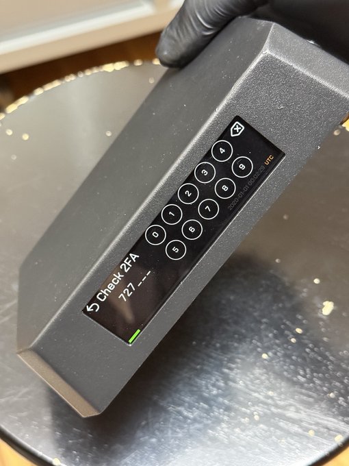 A gloved hand holds a dark gray "Check ZFA" electronic device with a numeric keypad and digital display, likely a security or authentication tool.