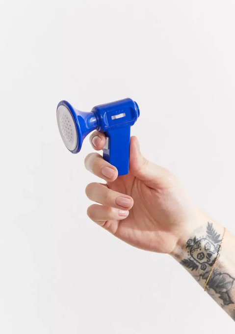 A hand with tattoos on the wrist holds up a small blue and white plastic spray bottle.