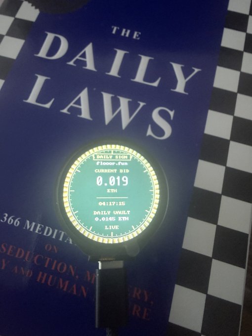 A small circular mining device displays "Daily Sign" with a current bid of 0.019 ETH and a daily vault of 0.0145 ETH, resting atop a copy of "The Daily Laws" book. The image illustrates the post's concept of a mining device designed to handle sign claims with NFTs, targeting wealthy investors willing to spend significant sums on the platform.