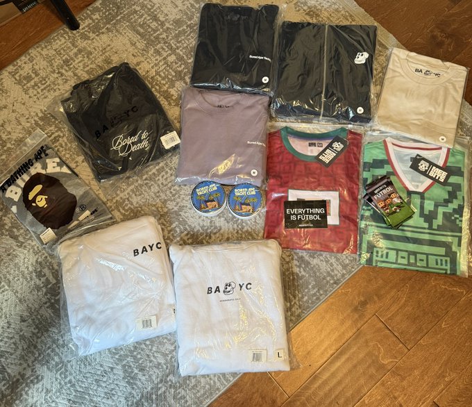 A collection of merchandise including BAYC (Bored Ape Yacht Club) shirts and hoodies, an "Everything is Futbol" jersey, green pixel-art style jersey, AF NYC apparel, and BAYC enamel pins, all laid out on a rug—showcasing a mail haul featuring BAYC and AF NYC gear as mentioned in the post.