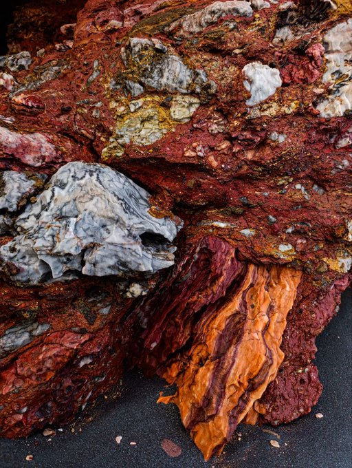 A close-up photograph of colorful textured rocks featuring rich red, white, and orange mineral formations.