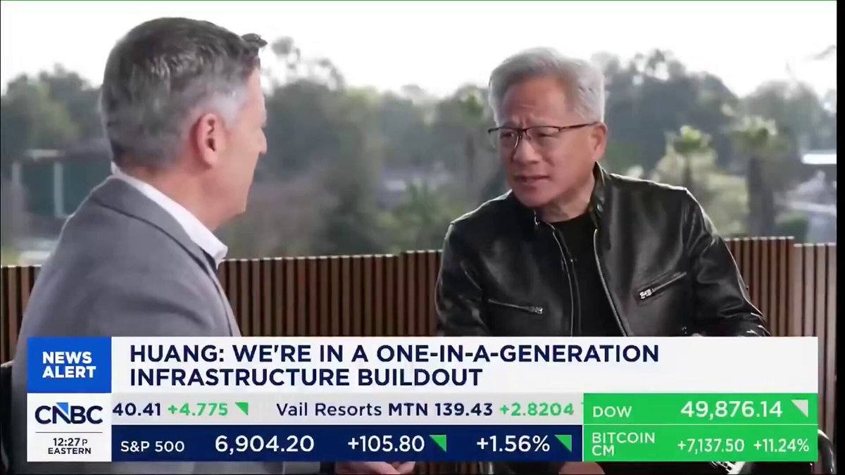 The image features a news segment with two men sitting at a table, engaged in conversation. The background of the scene includes trees, suggesting that they are in an outdoor setting. The main focus of the image is the discussion between the two men, who appear to be talking about something related to AI or technology.