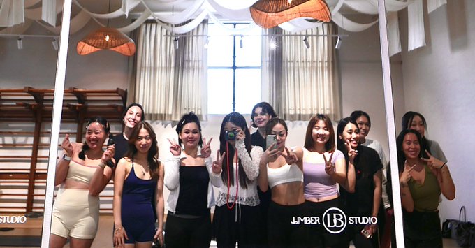 Group photo of about 12 women posing together at Limber LB Studio, making peace signs and holding phones, in a brightly lit dance/fitness studio space.