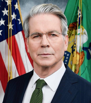 Official portrait of U.S. Treasury Secretary Scott Bessent, shown in a dark suit with a green tie, standing before the American flag and the Treasury Department seal. The image accompanies news of his announcement that OFAC has sanctioned digital asset wallets linked to Iran’s central bank, freezing over $130 million.