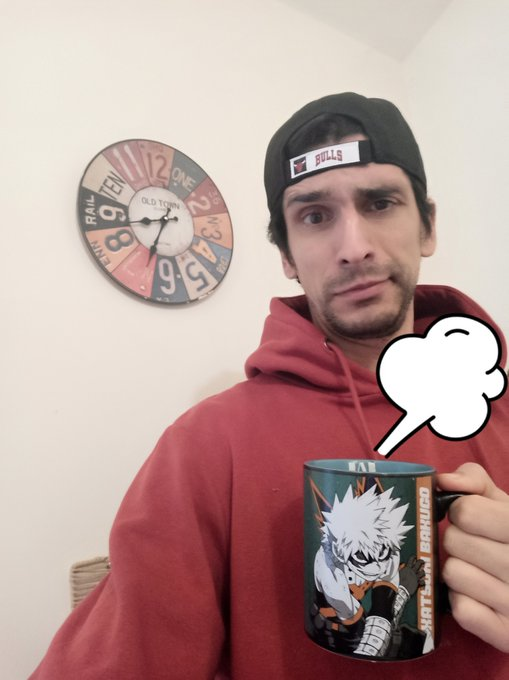 A man in a red hoodie and backward black 'BULLS' cap looks at the camera while holding a mug featuring Kakashi Hatake from Naruto; a cartoon thought bubble sits above the mug, and a decorative 'OLD TOWN' clock hangs on the wall behind him.
