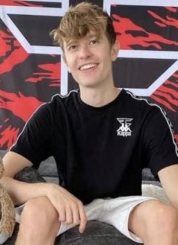 The image shows a young man with curly blonde hair smiling while sitting on a couch, wearing a black t-shirt featuring the "FaZe" logo. The post references "FAZE BLAZE," indicating this is likely FaZe Blaze, the trader highlighted as being up $24,000 in contrast to the top trader J7 who is down significantly.