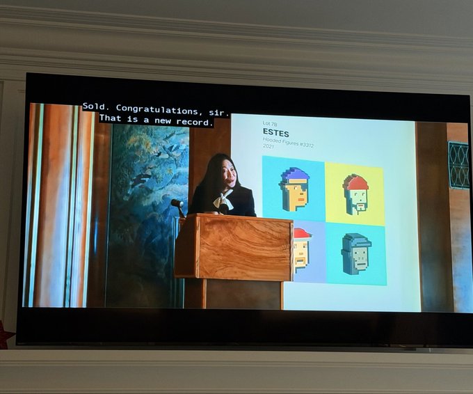 The image shows a television screen displaying an advertisement for PNC Bank featuring a woman giving a speech at a podium with a painting of four cartoon characters behind her, including two men and two women. The text on the screen reads "SOLD. CONGRATULATIONS. Sir That is a new record. ESTES".