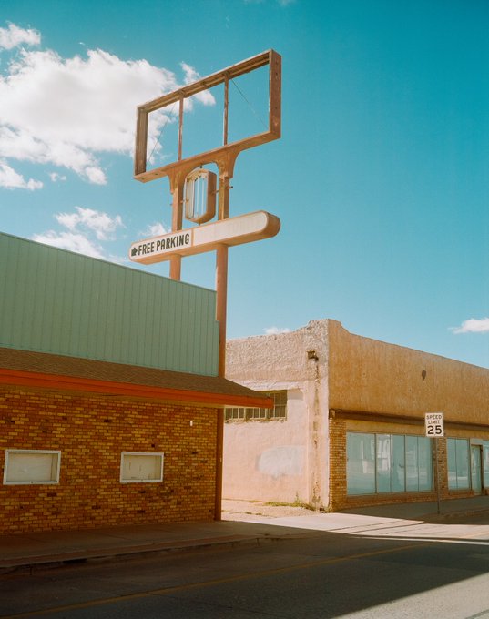 iced coffee shop with a green roof and white sign, "FREE PARKING" on a brown pole, and a brick building with a red door and window.