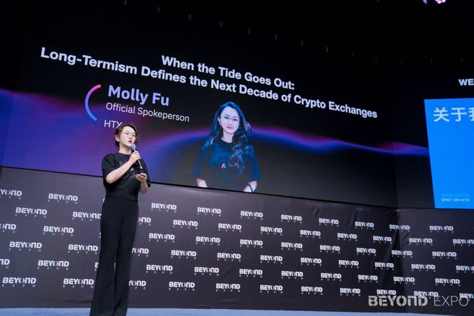 The image features a woman standing on stage, giving a speech or presentation. She appears to be addressing an audience at an event, possibly related to cryptocurrency or blockchain technology. The background of the image includes text that reads "long-termism defines the tide goes out when the tide goes out", which could potentially be a metaphor for the concept of cryptocurrency exchanges going out with time.

The post also mentions Molly, who is likely the speaker at this event. She is described as an Asian woman giving a speech on stage. The image does not provide any specific information about the content of the speech or the context in which it took place.