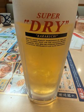 A tall glass of Asahi Super 'Dry' Karakuchi beer sitting on a restaurant table with a paper menu underneath.