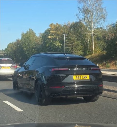 The rear view of a black Lamborghini Urus driving on a highway, bearing the license plate 'R88 AMW'.