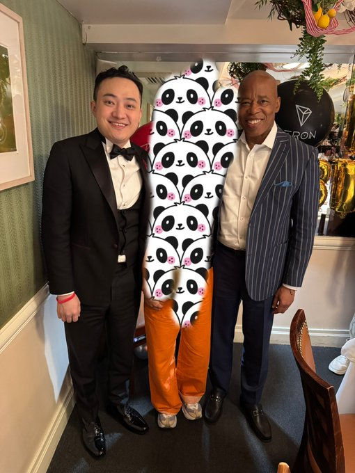 The image shows two men standing next to each other with their arms around another man who is holding a panda-themed sign or board game, possibly for an event or promotion related to the blockchain ecosystem. The scene takes place in front of a dining table, suggesting that they might be at a restaurant or gathering.
