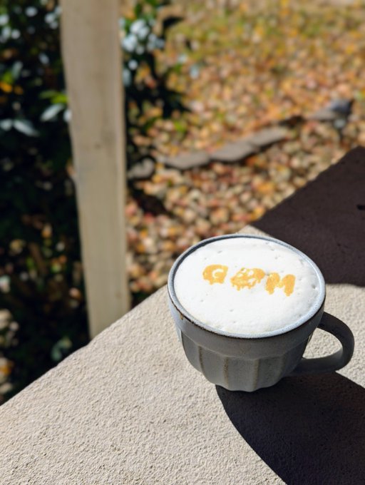 A frothy cappuccino with "C&M" written in caramel sits on a sunny ledge, accompanied by a warm "Good morning my friends" greeting.